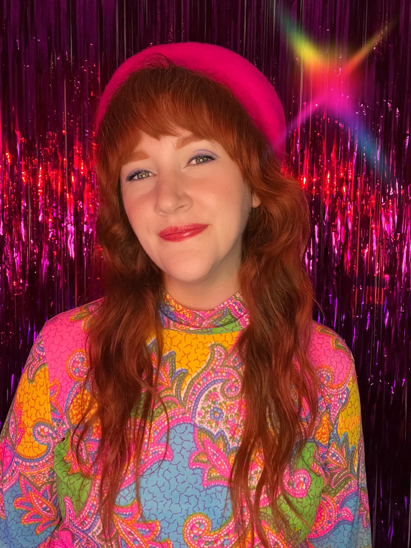 Allison in vintage dress and pink beret, in front of rainbow backdrop