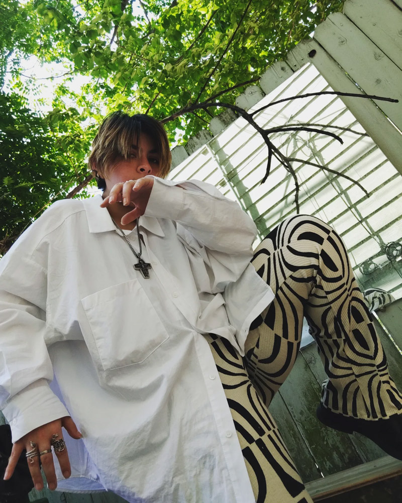 Chey in front of trees, wearing large white shirt and bold patterned pants