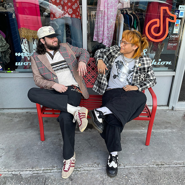 2 people sitting on a bench in front of Buffalo Exchange