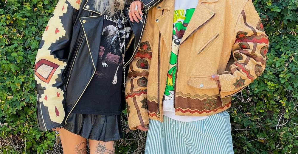 Two people posing outside in vintage leather jackets with western cutouts, styled with modern accents like graphic tee shirts and chunky silver jewelry