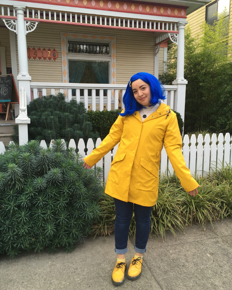 13 Buffalo Employee dressed in yellow raincoat with blue hair standing outside of a victorian house.