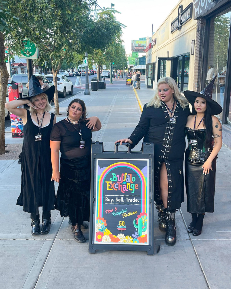 7 Group of people in all black witch outfits posing next to Buffalo Exchange sandwich board