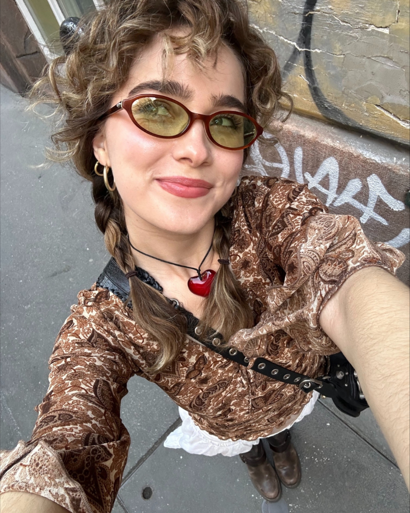 Photo of actor Haley Lu Richardson wearing sunglasses and a patterned brown blouse