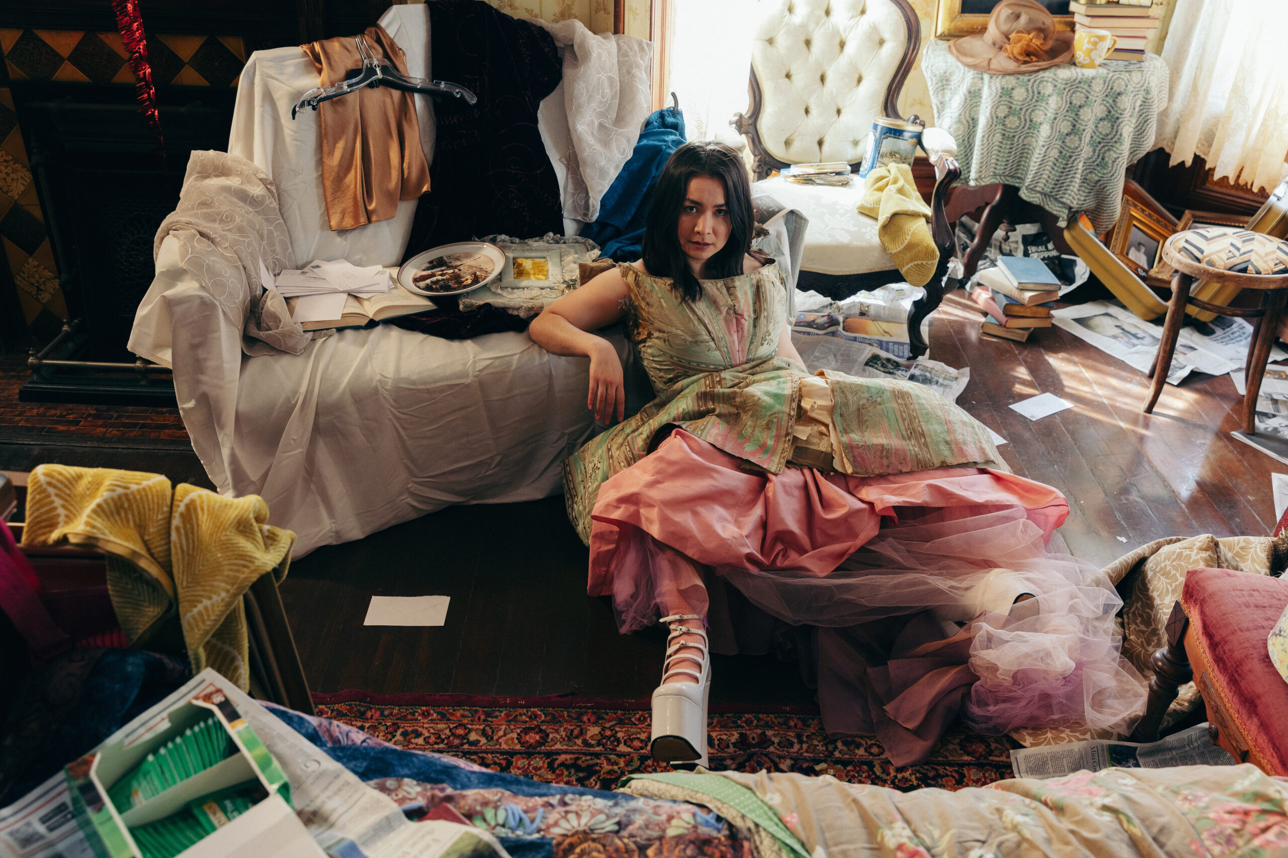 Singer Songwriter Mitski wears ornate vintage dress while sitting in densely decorated room