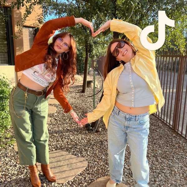 Two employees in trendy, contemporary fall outfits posing with their arms forming the shape of a heart, with TikTok logo overlay