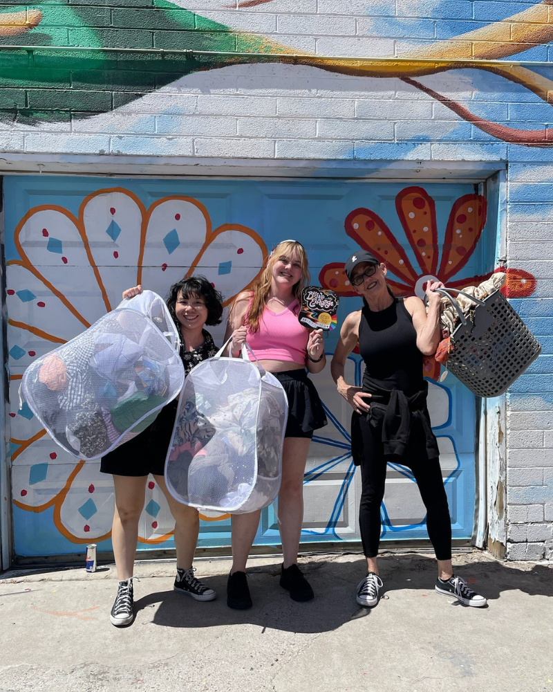 Three $1 Sale customers holding up laundry bags full of clothing.