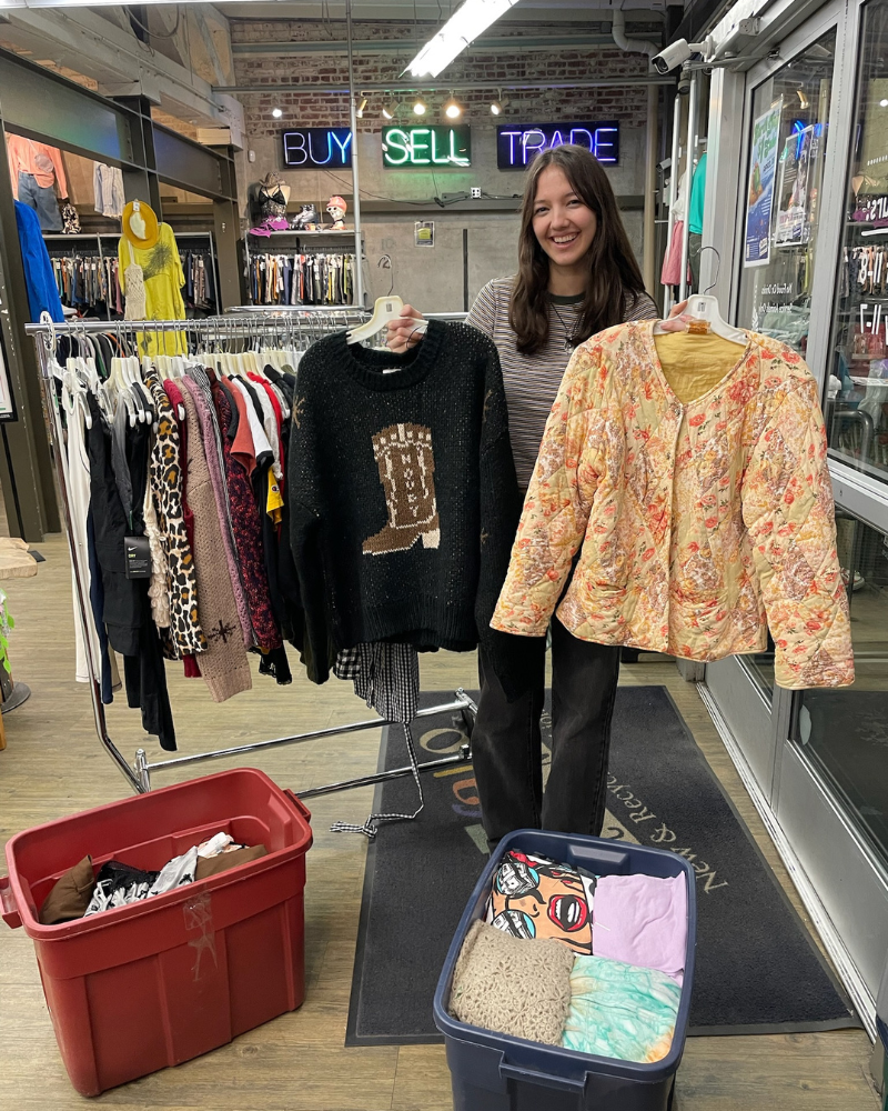 Buffalo Exchange employee smiling and holding up two clothing items for the $1 Sale.