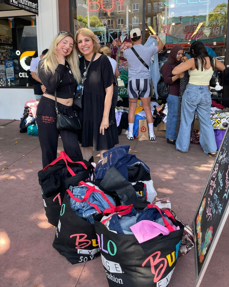 $1 Sale customers smiling and posing next to several bags of clothes.