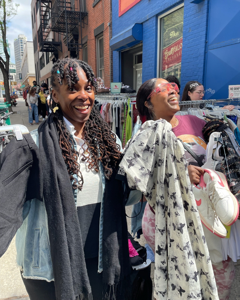 $1 Sale customers laughing and holding up finds from the sale.