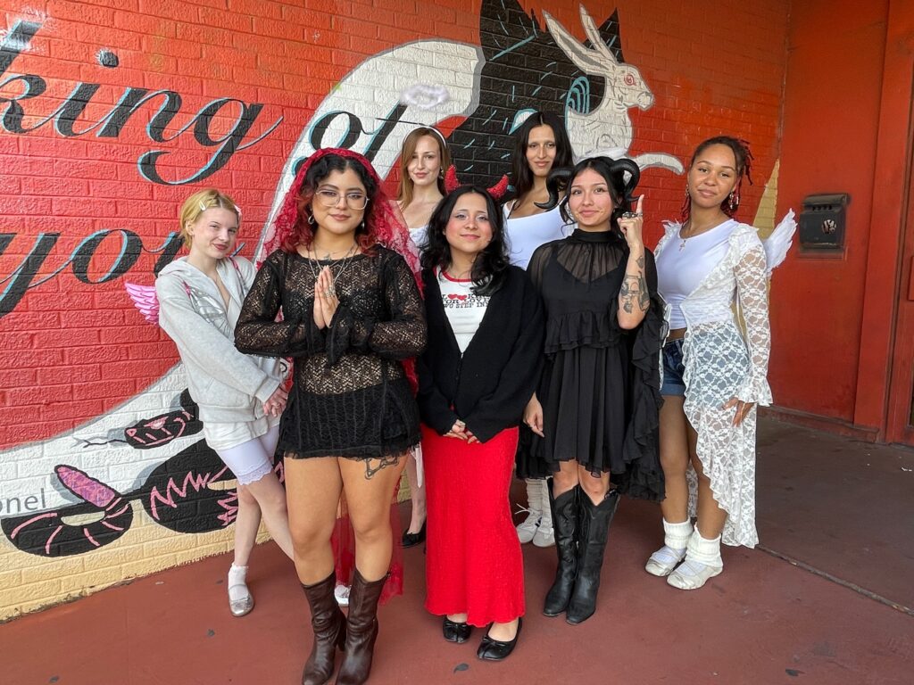 A group of people poses in their Halloween costumes, half of them dressed up as devils and the other half as angels